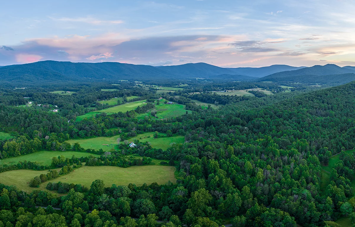 rural and forested land under blue mountains during sunrise