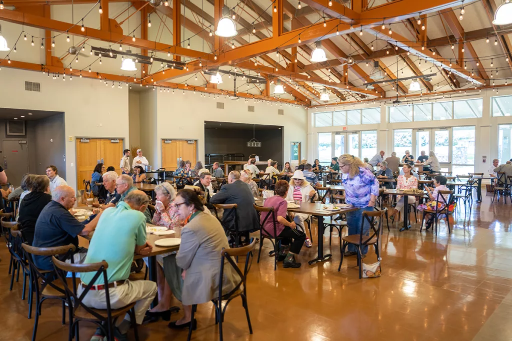 attendees sit at tables in a bright lit room eating lunch