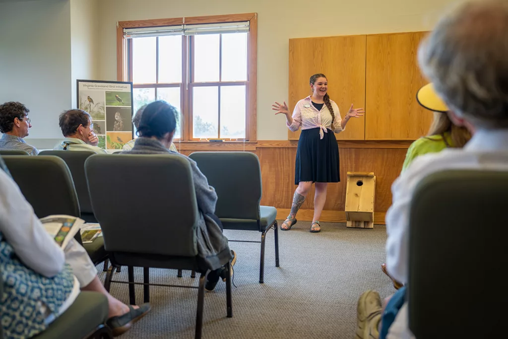 a woman with a bird box presents in front of a crowd