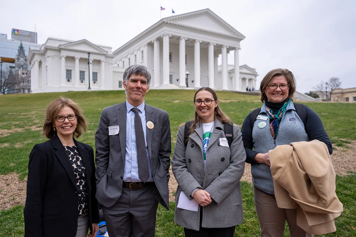 Four staff stand in front of the Virginia State Capitol building and lawn.