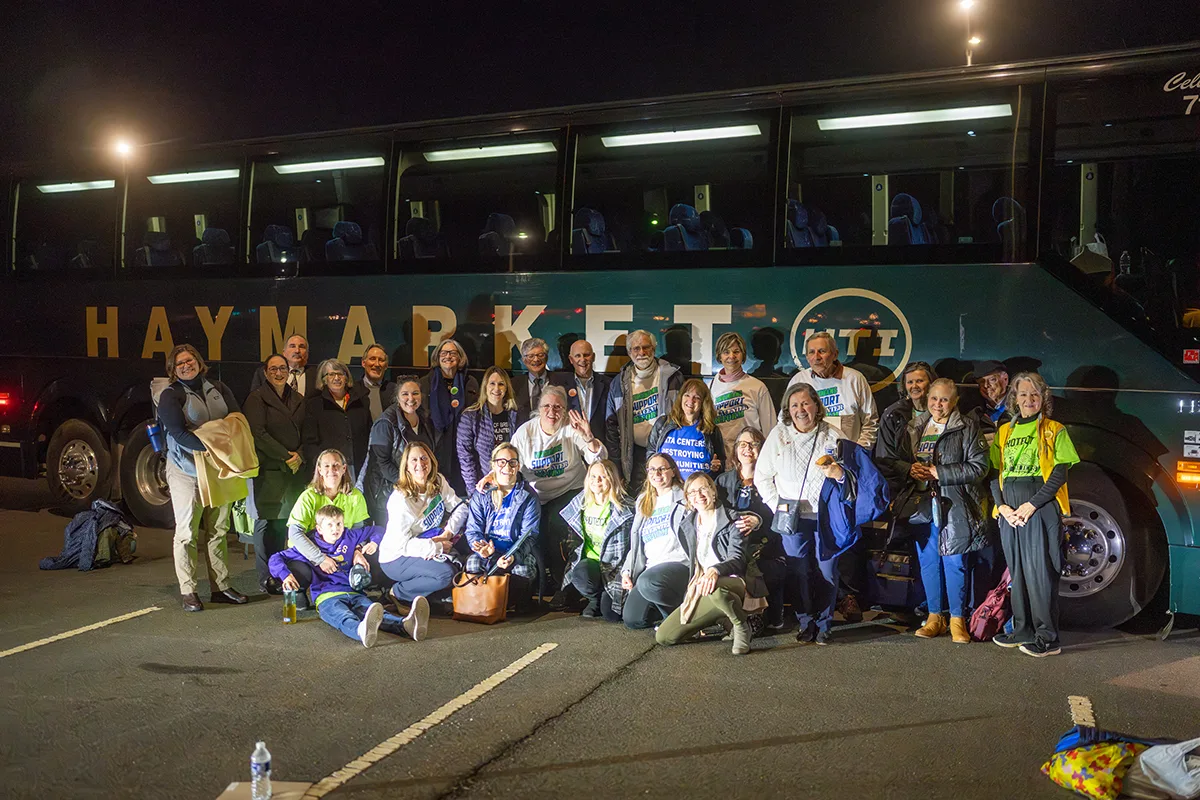 a large group sits and stands outside a bus before sunrise