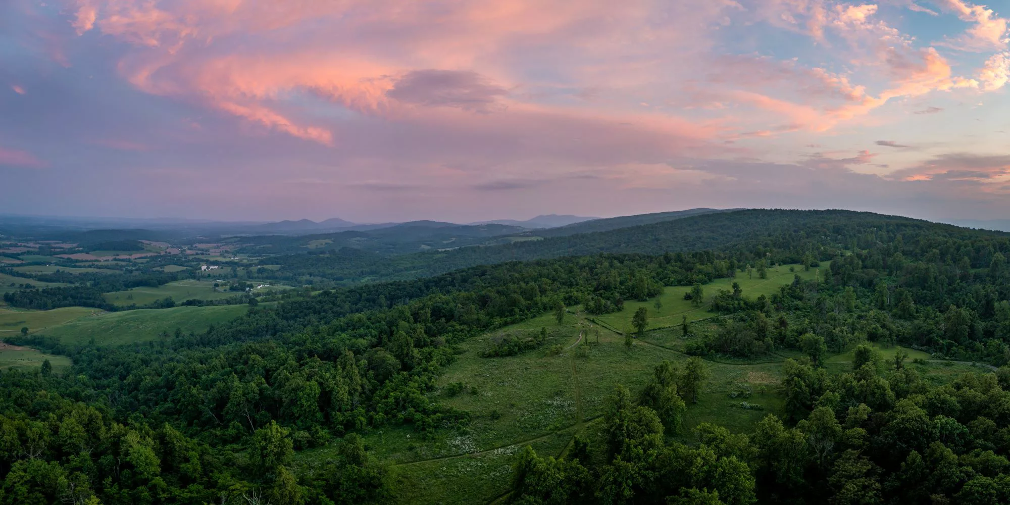 aerial image of a green patch of land surrounded by forest, during sunset