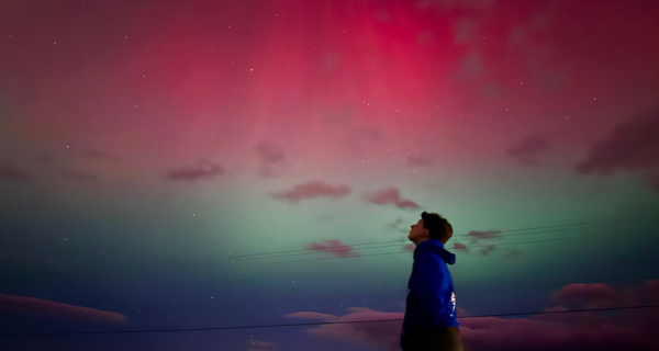 A figure looking at the night sky where the aurora is visible.