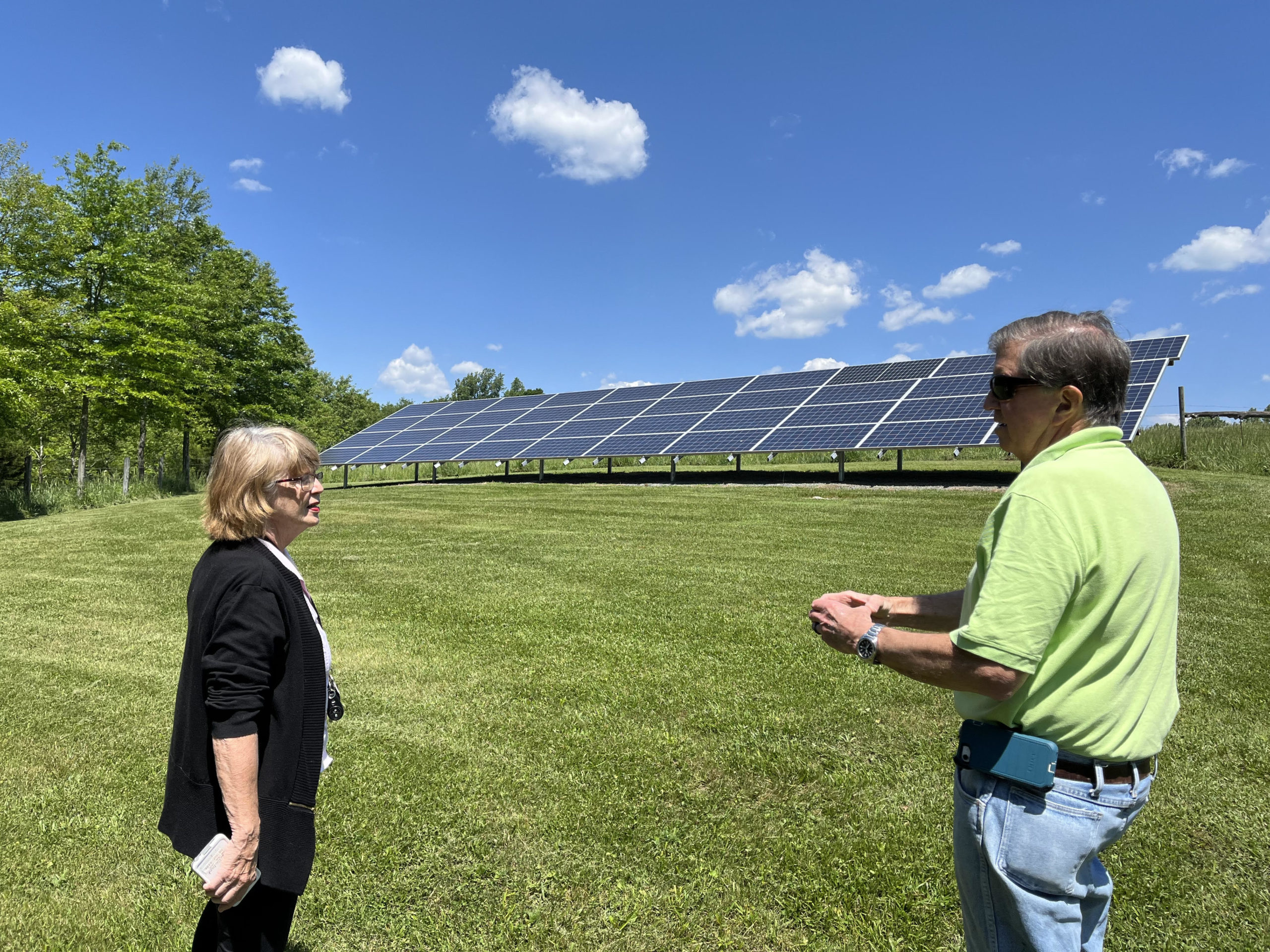 a man and woman stand on a lawn in front of a ground-mounted solar array