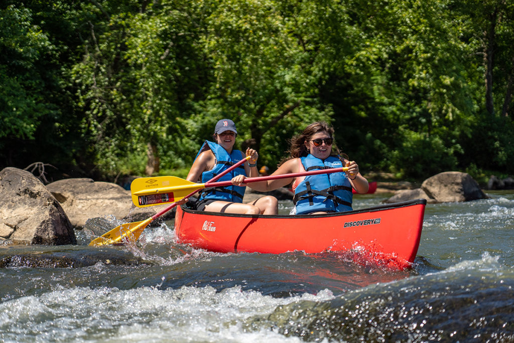 two young women paddle over rapids in a canoe