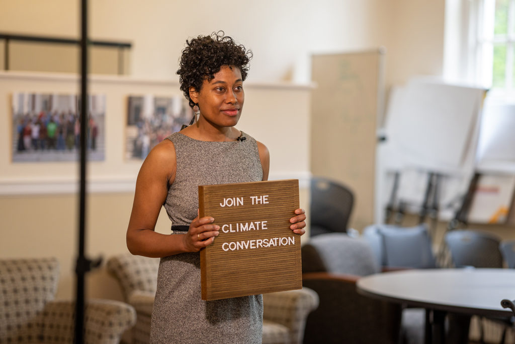 a Black woman holds a wooden sign that says "Join the climate conversation"
