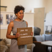 a Black woman holds a wooden sign that says "Join the climate conversation"