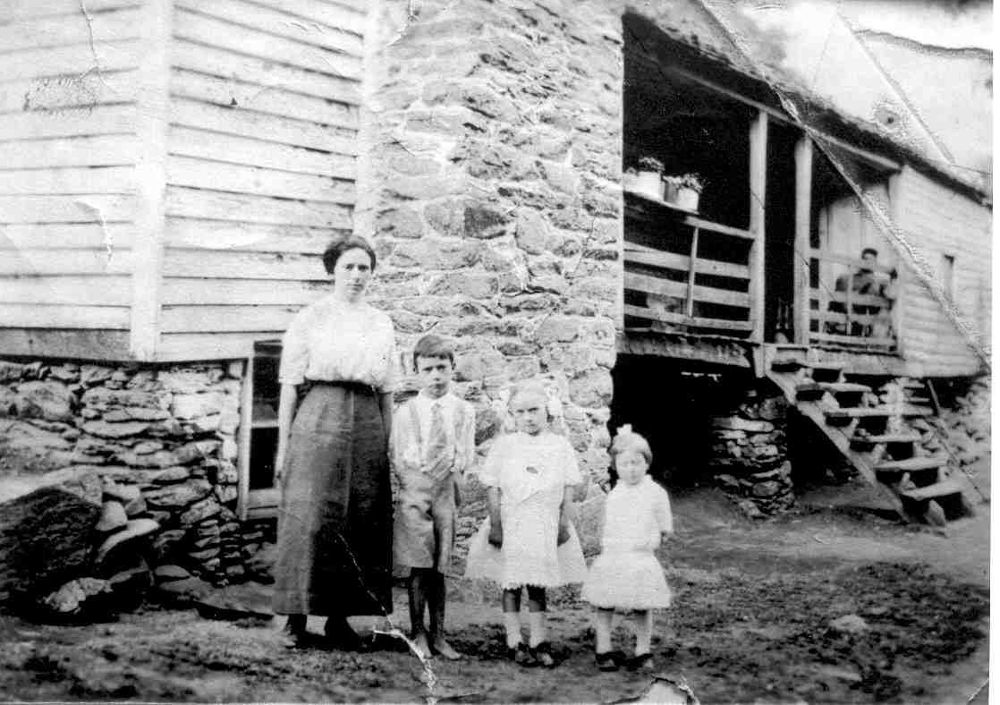 black and white historic image of a mother and three children in front of a house