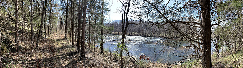 A trail through the woods next to a blue river