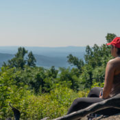 two young people sitting on rocks looking at a valley of blue mountains during the summertime