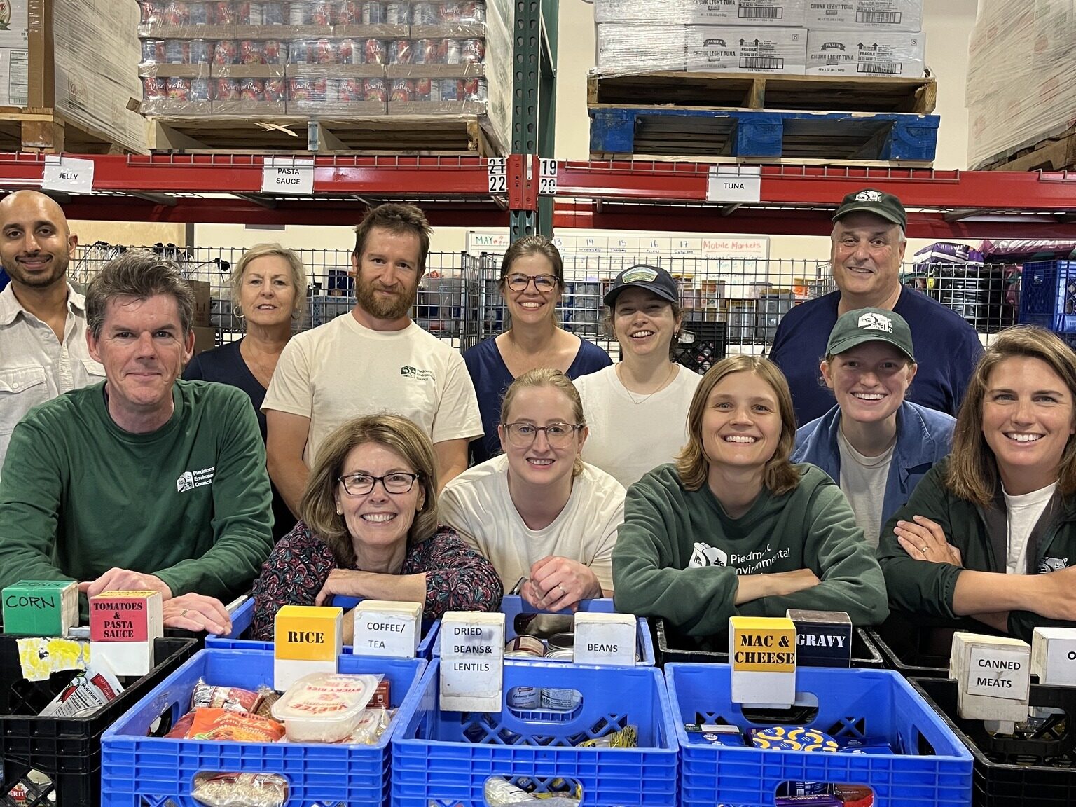Piedmont Environmental Council staff stand behind crates of sorted food in a warehouse, smiling at the camera.