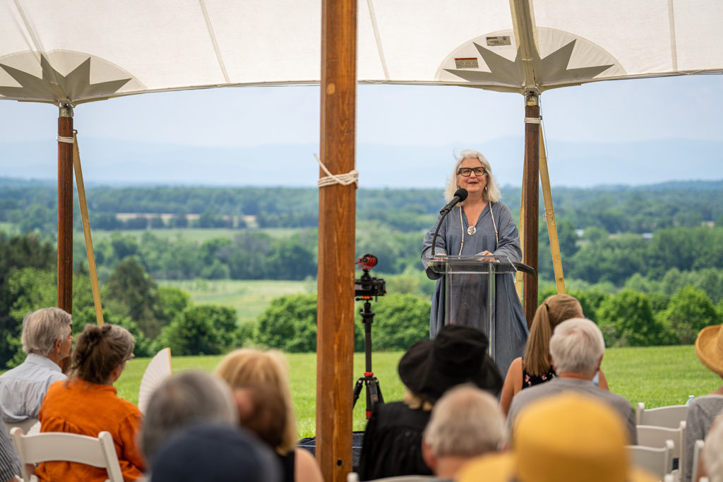 a women speaks at a podium under a tent, to a crowd