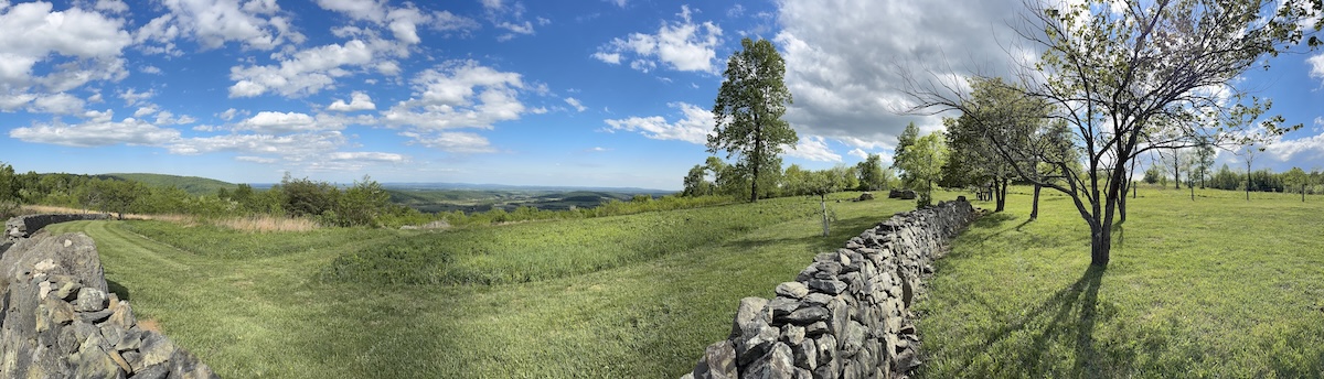 A panoramic view of an overlook into a valley beyond, bordered by a stone wall.
