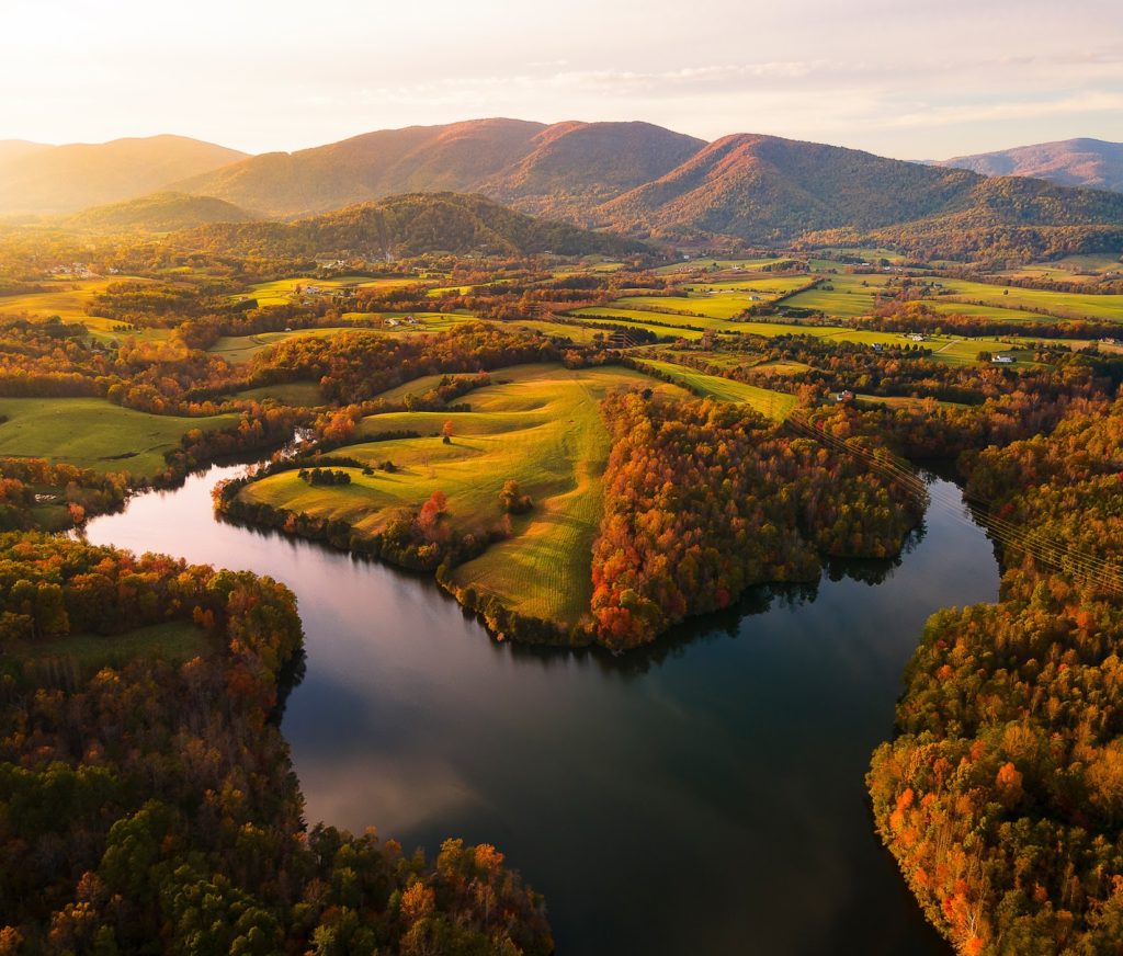 sunset over a reservoir surrounded by autumn forests, green pastures and rolling mountains