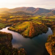 sunset over a reservoir surrounded by autumn forests, green pastures and rolling mountains