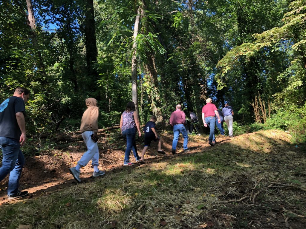 a group of neighbors walk up a sloped, forested trail