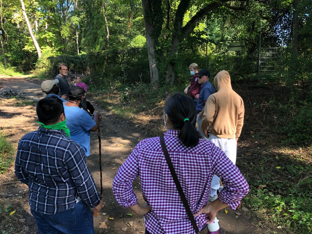 a group of neighbors stand in a circle chatting on a dirt trail