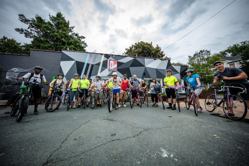About 20 people pose with bikes in front of the Bridge Progressive Arts Initiative building in 2018.