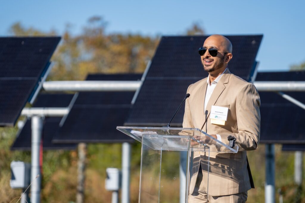 Ashish stands at a podium in front of the solar panels at PEC's agrivoltaics installation.