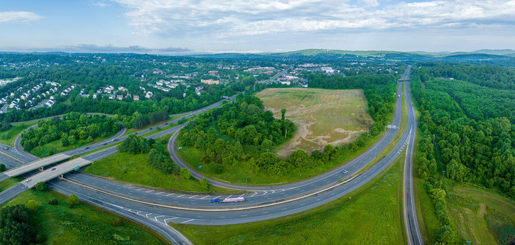 aerial image of an empty lot with trees along a highway interchange