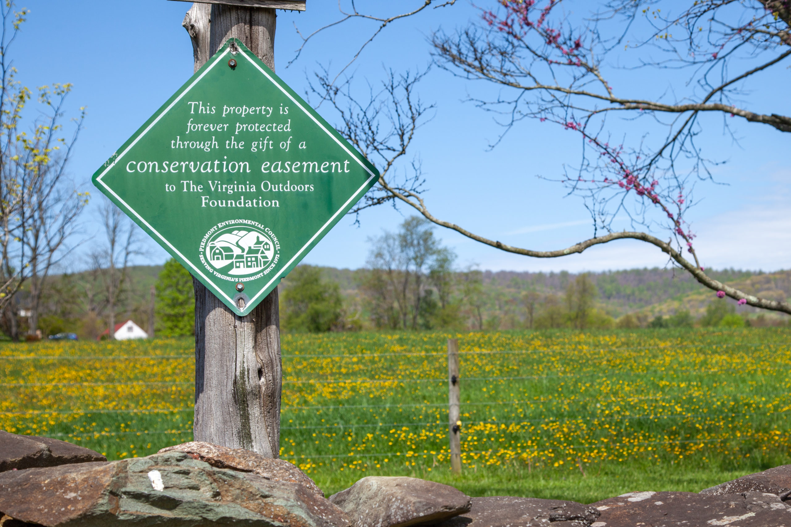 a green conservation easement sign on a fence, with field behind