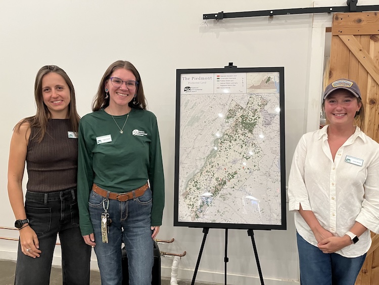 Three people standing next to a map on an easel.
