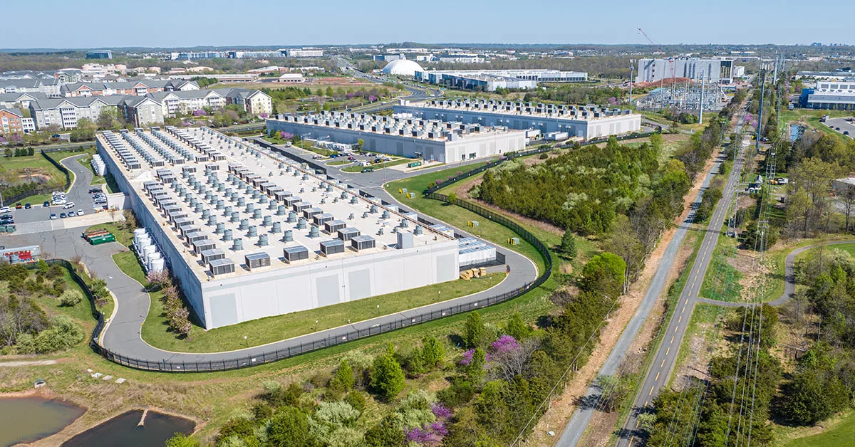 aerial view of a few huge data center buildings between a set of apartments and public trail