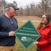 a man and women hold a green sign between them that says "This property is forever protected with a conservation easement"