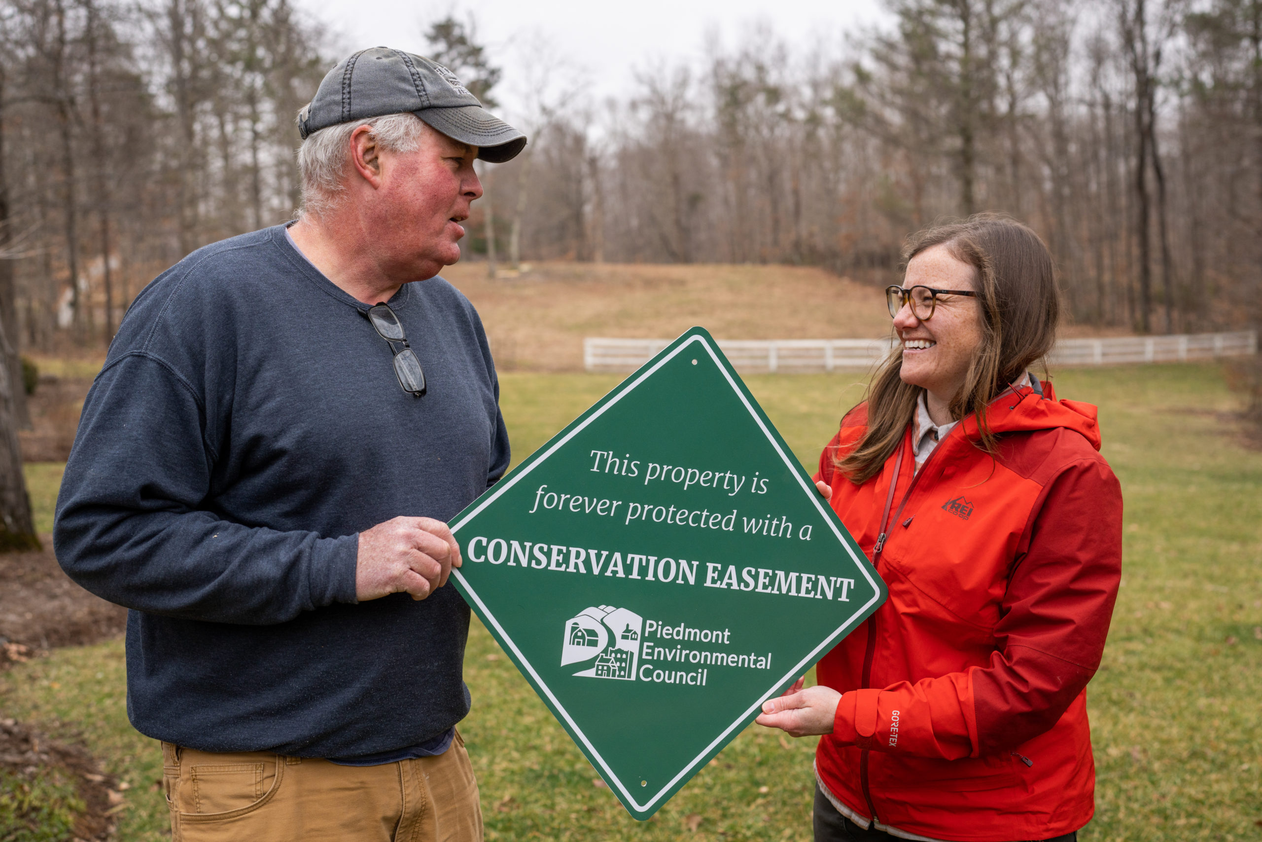 a man and women hold a green sign between them that says "This property is forever protected with a conservation easement"