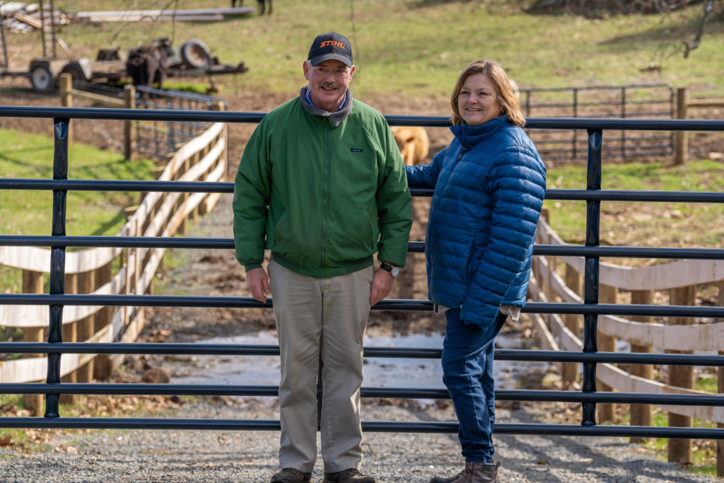 a couple stands at a fence on the farm