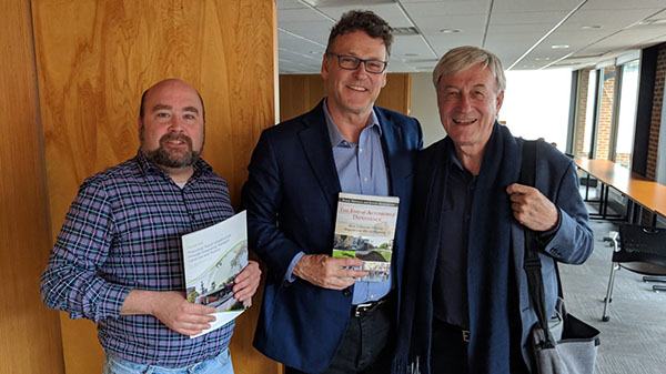 Three men pose holding books.