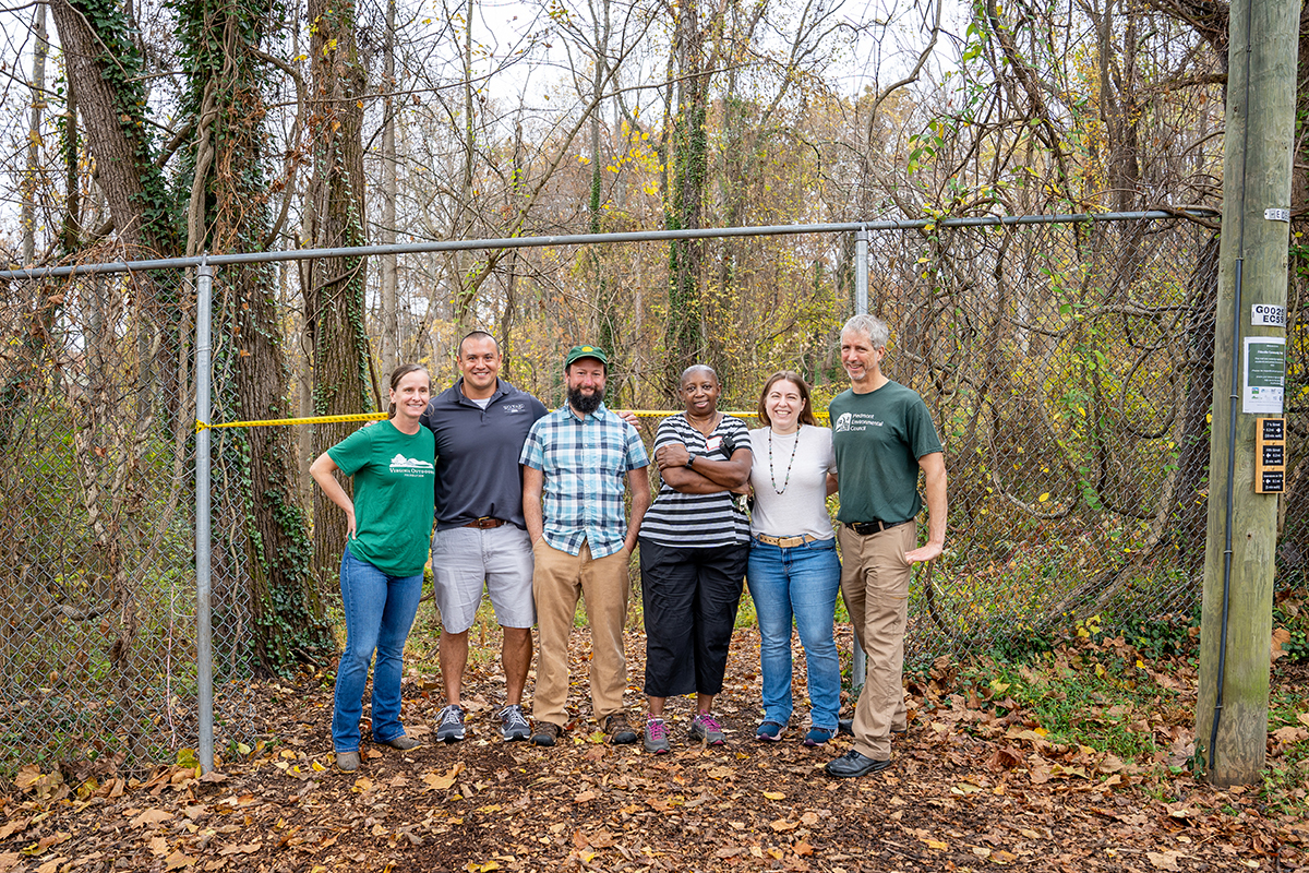 a group of six stand in front of a trail entrance