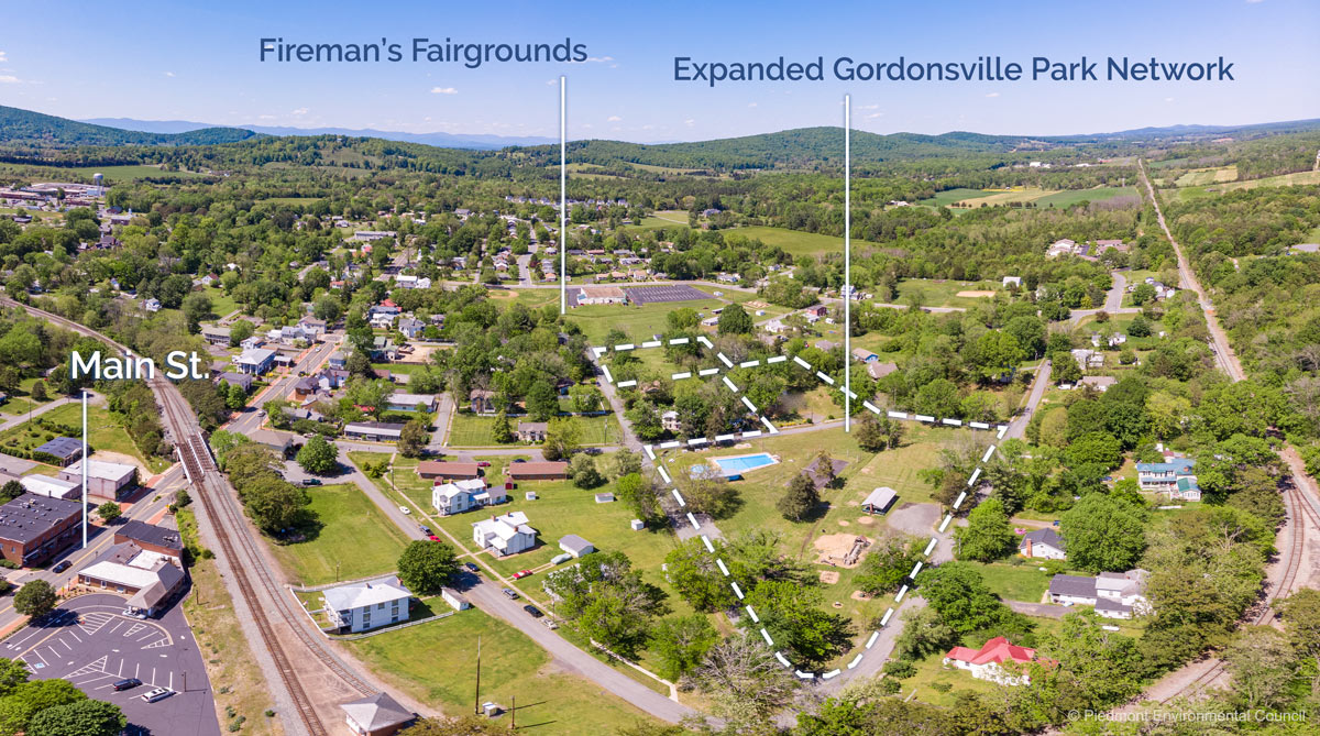 Aerial shot of Gordonsville. Main Street on the left and Verling Park with its swimming pool in the middle in the middle interspersed with trees, houses and buildings. Mountains can be seen in the distance.