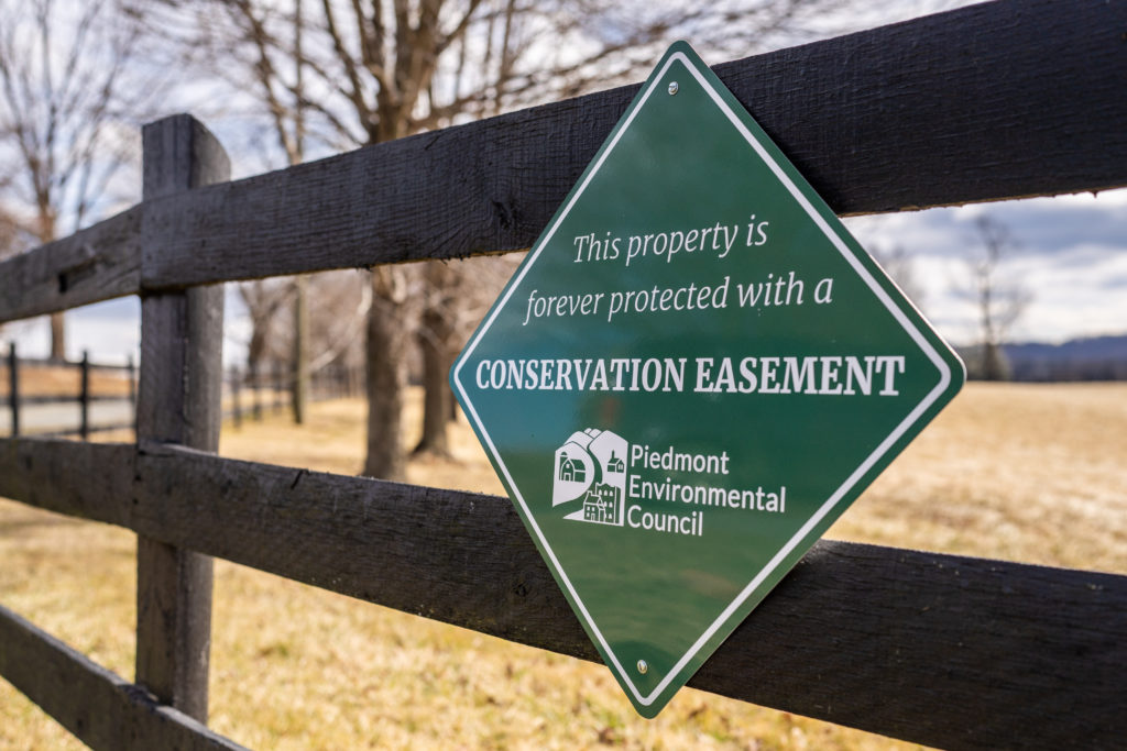 a green sign that says "This property is forever protected with a conservation easement" on a fence