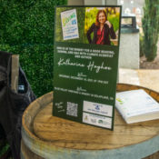 a poster for the event and a copy of Saving Us sits on top of a wine barrel