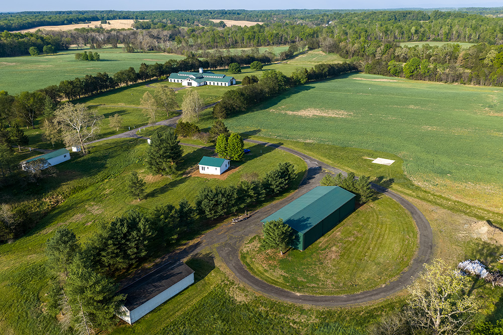 Aerial view of a farm with green rooftops surrounded by green grass and trees.