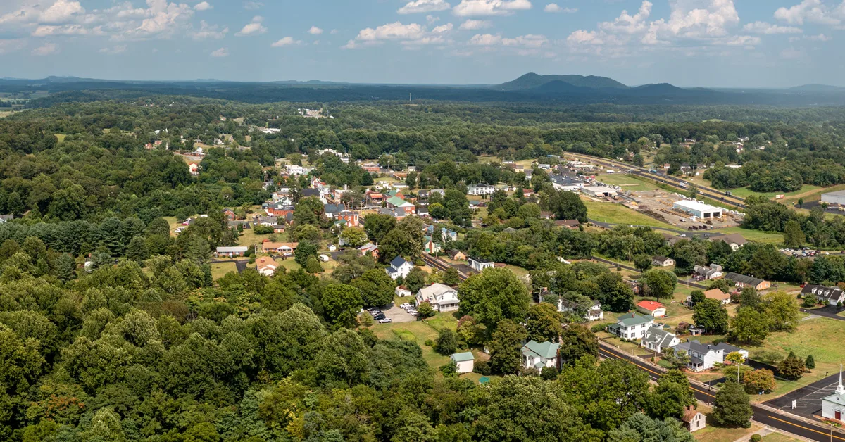 drone shot over green trees and main street with houses and buildings with mountains in the distance