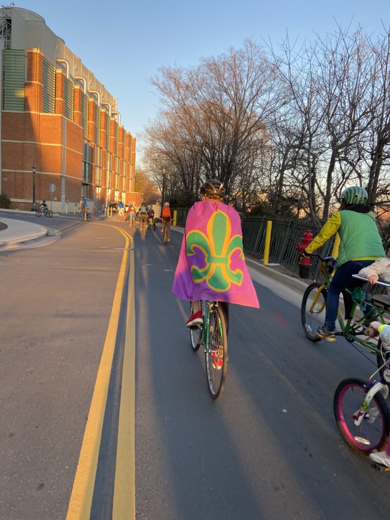 person riding on a bike down a street with a mardi gras themed cape