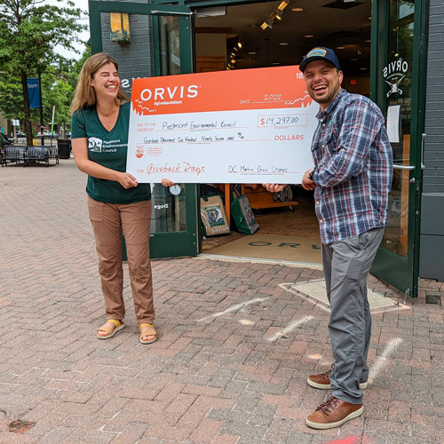 woman and man holding a big check outside an orvis store