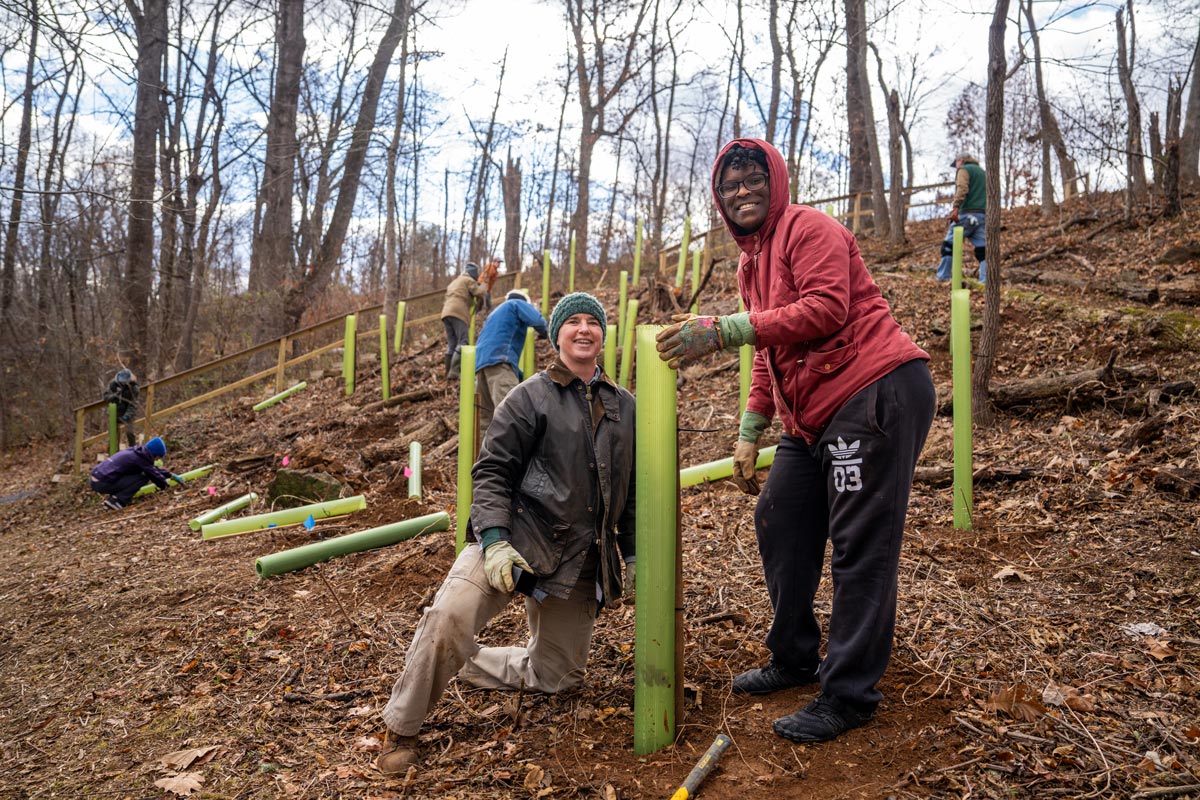 Two male volunteers smiling at camera while planting trees on a hillside.