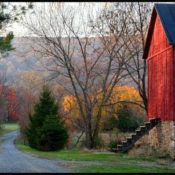 an old red building situated next to a gravel road, with fall foliage in the background