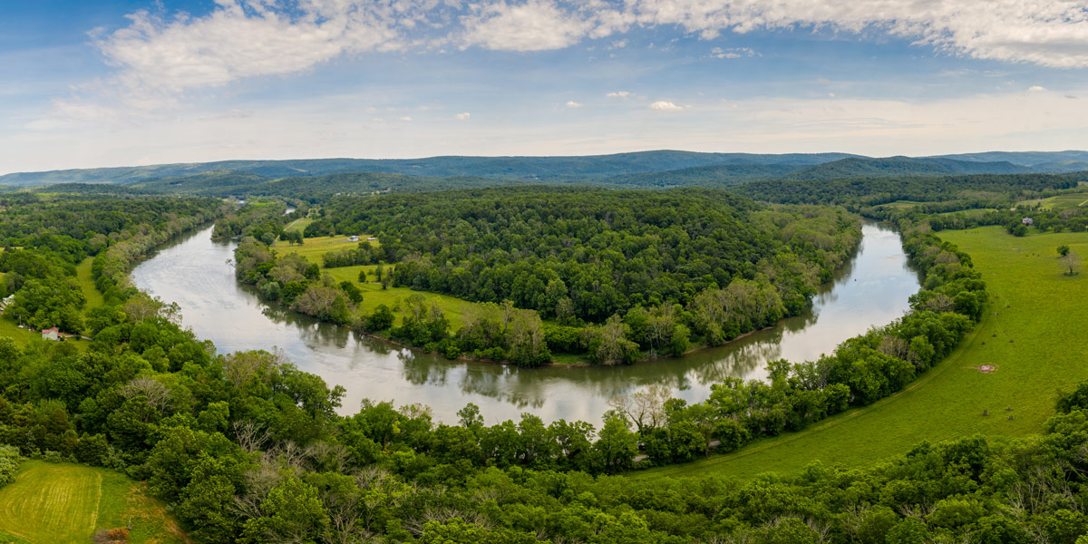 drone photo of a river surrounded by trees and landscape with hills.