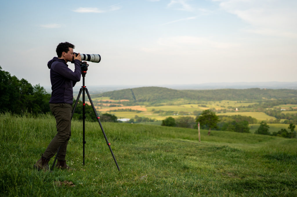 A man photographs a meadow with a telephoto lens.
