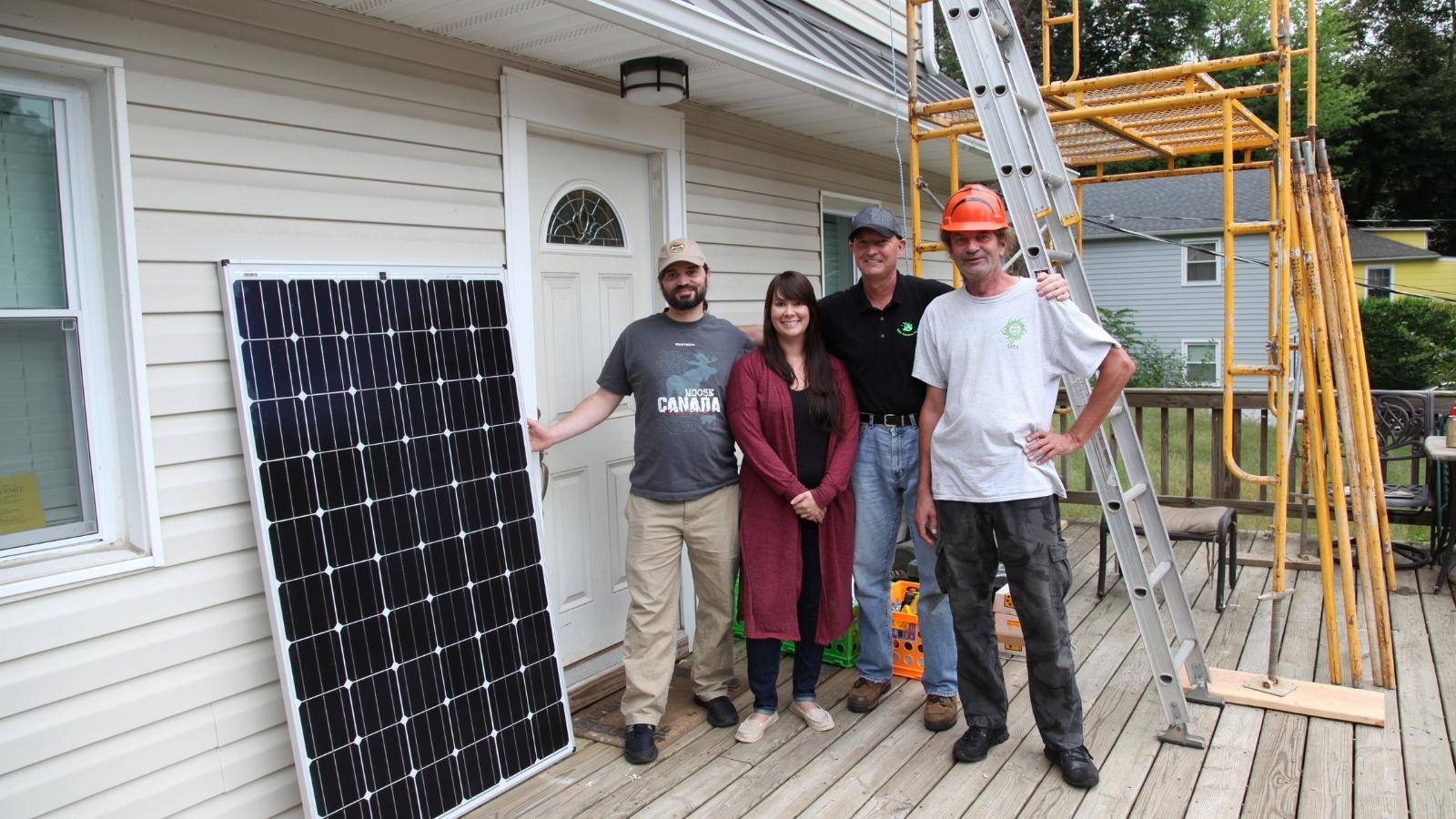 couple stands with two solar installers next to solar panel