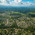 aerial image of suburban neighborhoods surrounded by green forest canopy, blue mountains and cloudy skies