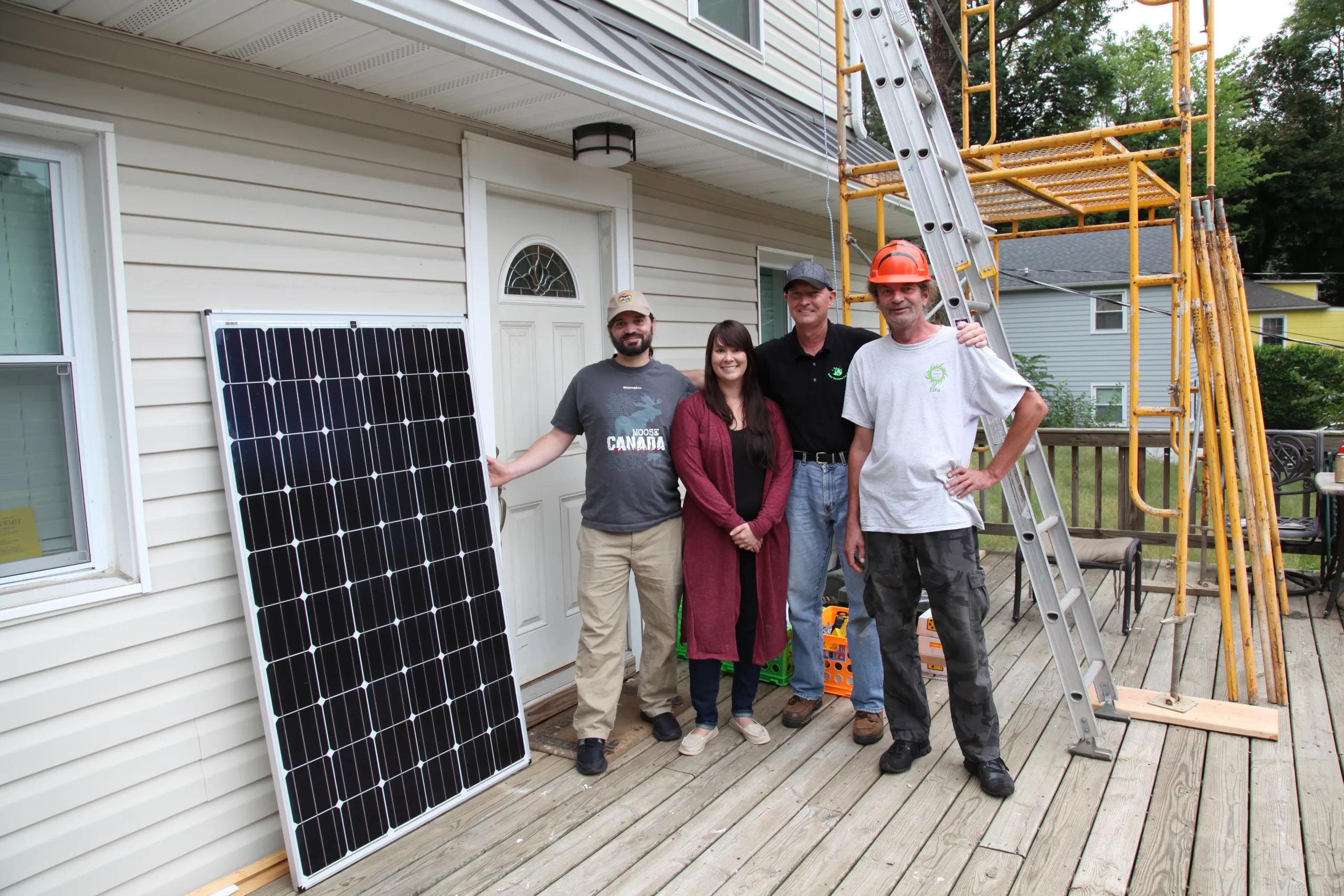 a couple stands with two solar installers and a solar panel in front of a home