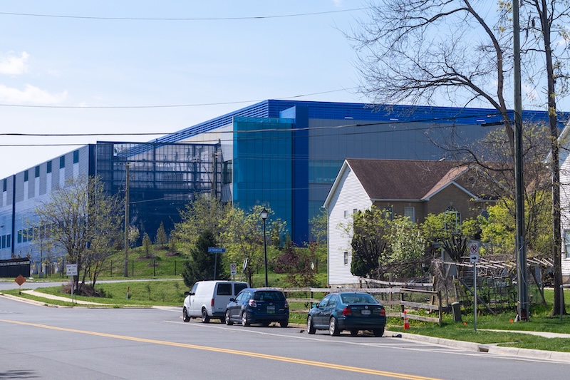 A large data center in the background sits directly across the street from a residential neighborhood in the foreground.